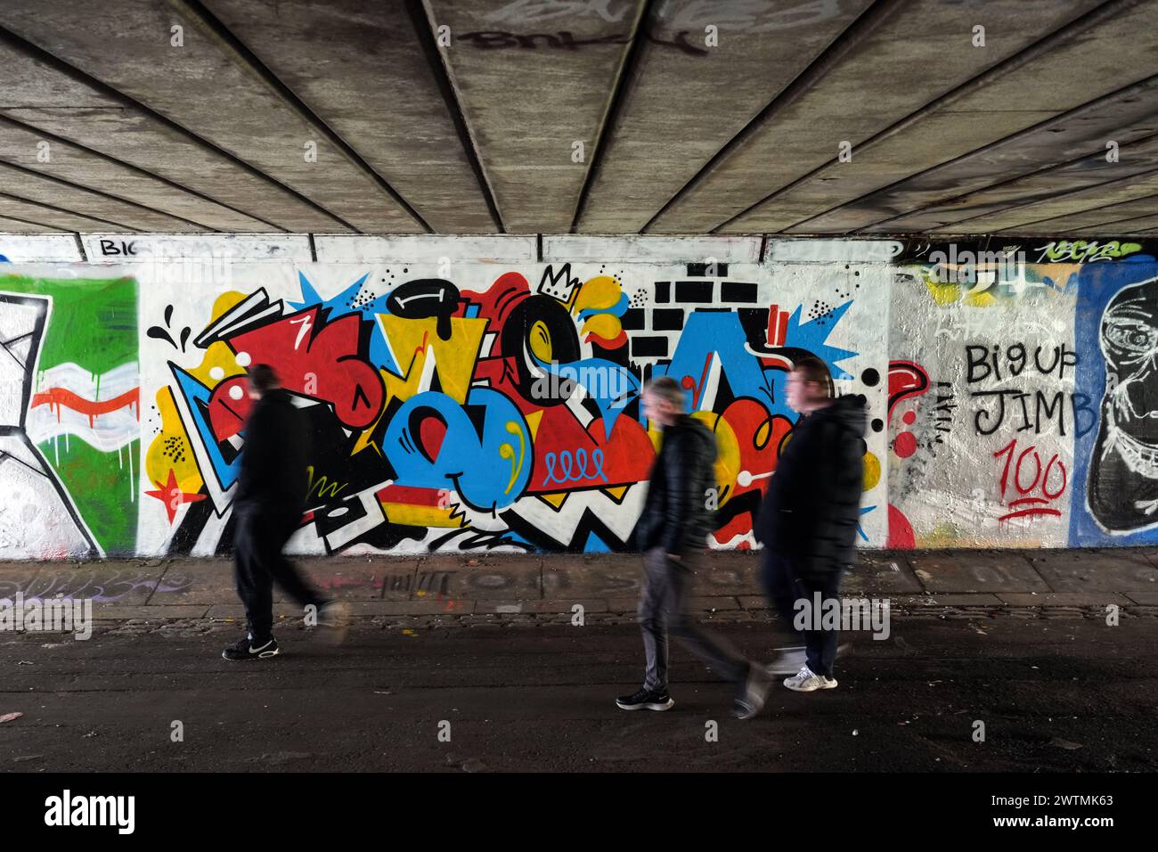 People walk past a graffiti mural under a bridge in Glasgow, Scotland. Stock Photo