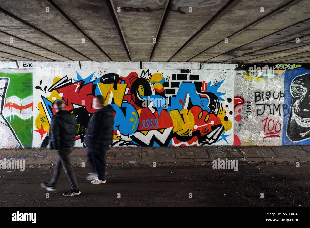 People walk past a graffiti mural under a bridge in Glasgow, Scotland. Stock Photo