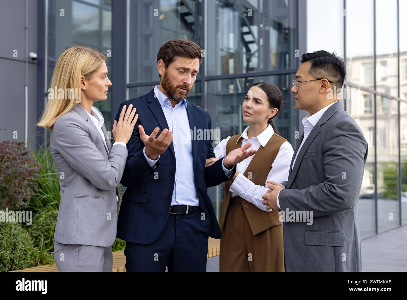 Sympathetic coworkers gathering around sad caucasian man with spread arms and looking at colleague with sorrow. Pity manager telling about unsuccessful results and being scared about getting fired. Stock Photo