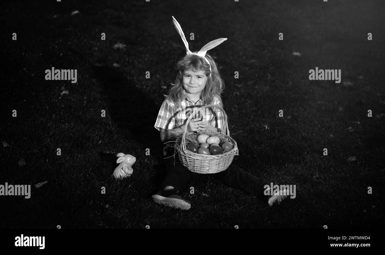 Child with easter eggs in basket outdoor. Boy on grass in park. Easter egg hunt. Fynny kids portrait. Cute bunny child with rabbit ears. Stock Photo