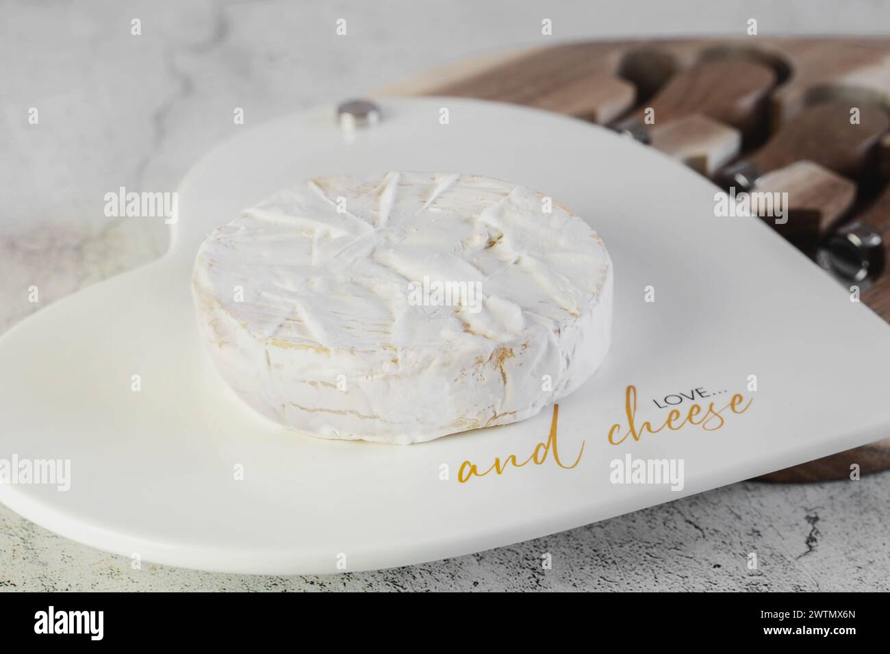 soft cheeses with white mold on a white board. A round small head of brie or camembert cheese. A set of knives and a cheese board on a light backgroun Stock Photo