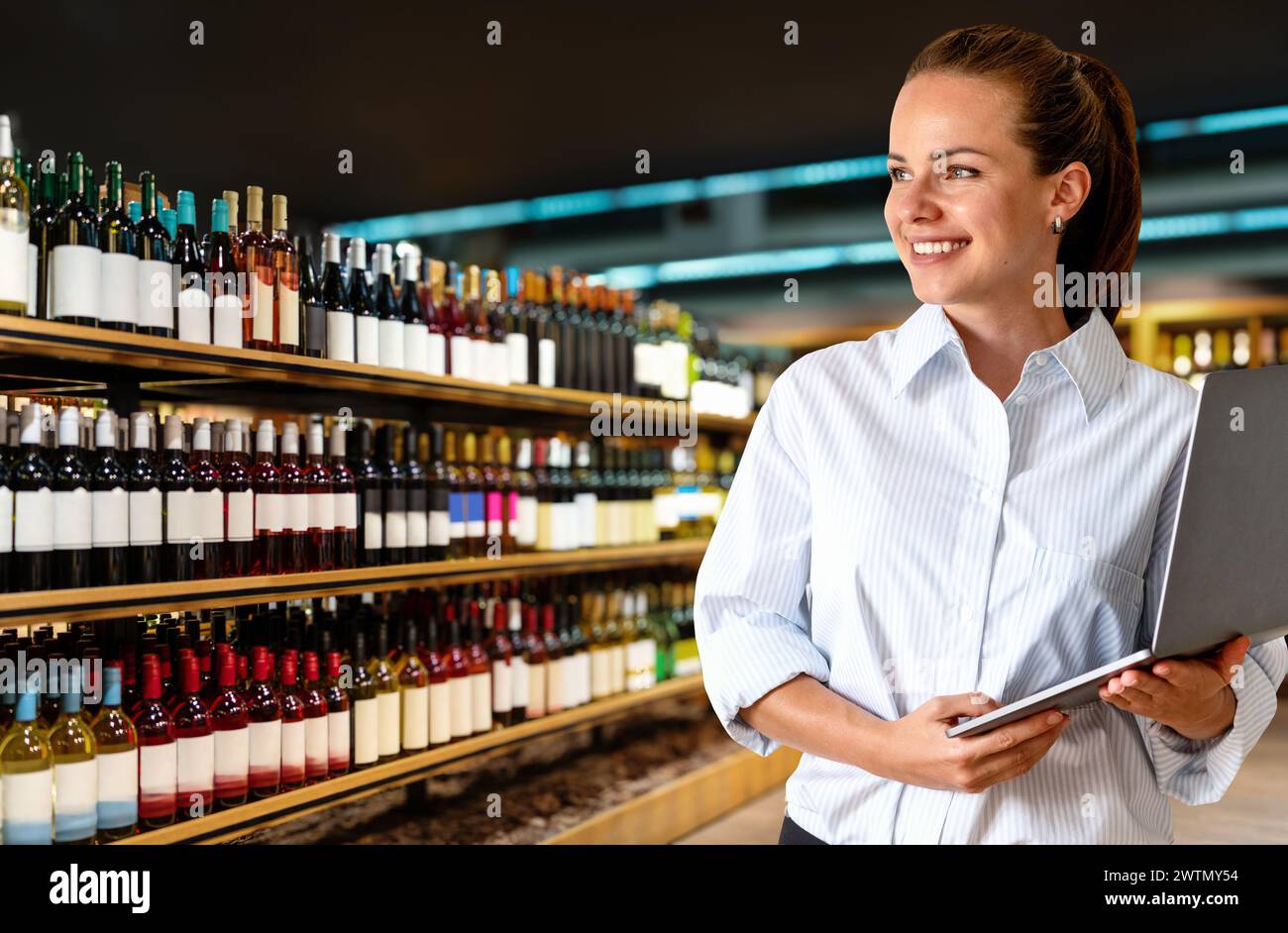 Pretty businesswoman with laptop in her hands stands in liquor store salesfloor. Stock Photo