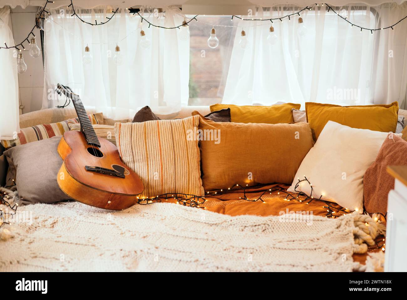 Cozy bedroom interior inspired by autumn colors. Pillows, light bed of a mobile home on wheels. Light bulbs. Stock Photo