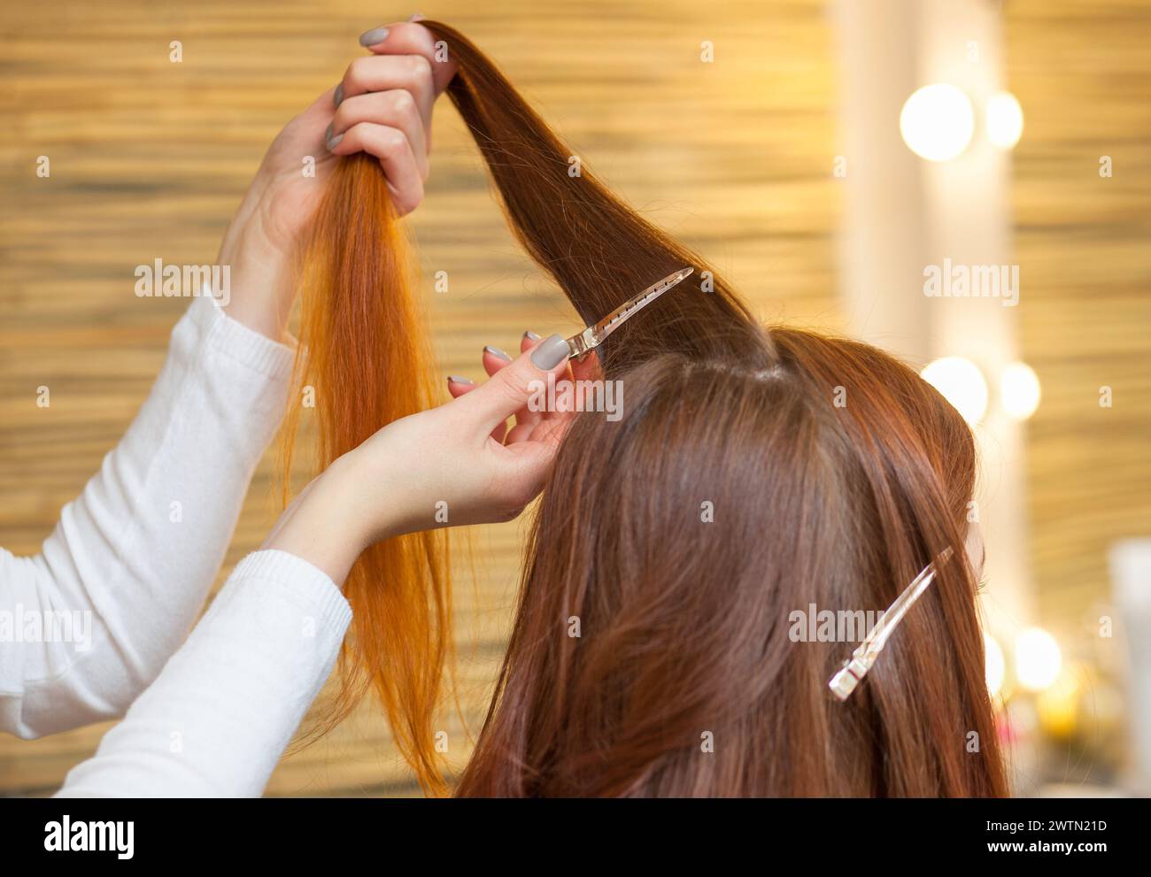 Hairdresser combing her long, red hair of his client in the beauty salon. Professional hair care and creating hairstyles. Stock Photo
