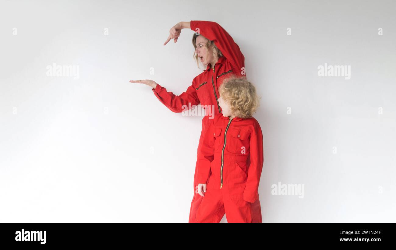 A positive blonde with a young son in red jumpsuits points to the place where your advertising text is displayed, standing out against a white backgro Stock Photo