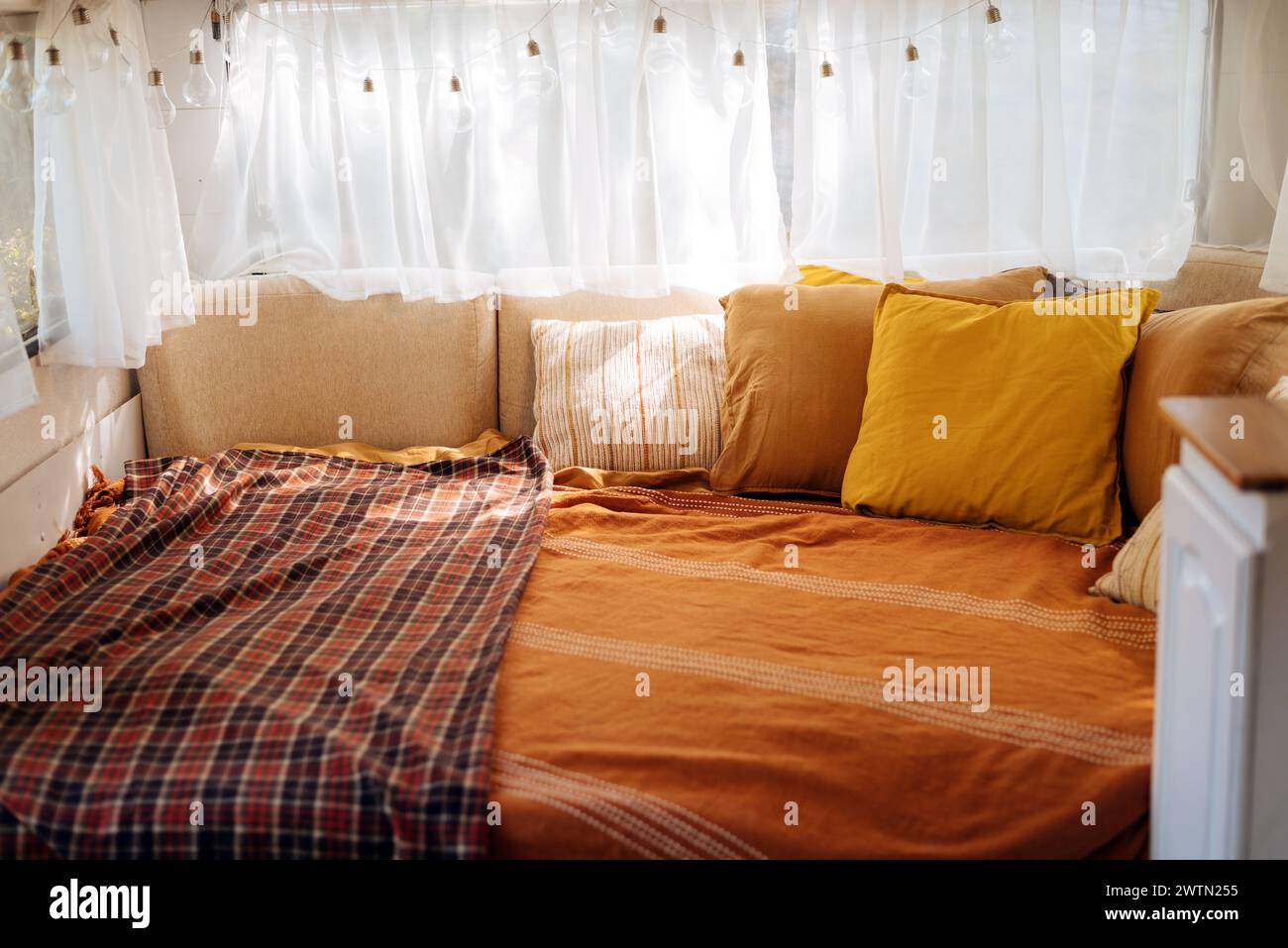 Cozy bedroom interior inspired by autumn colors. Pillows, light bed of a mobile home on wheels. Light bulbs. Stock Photo