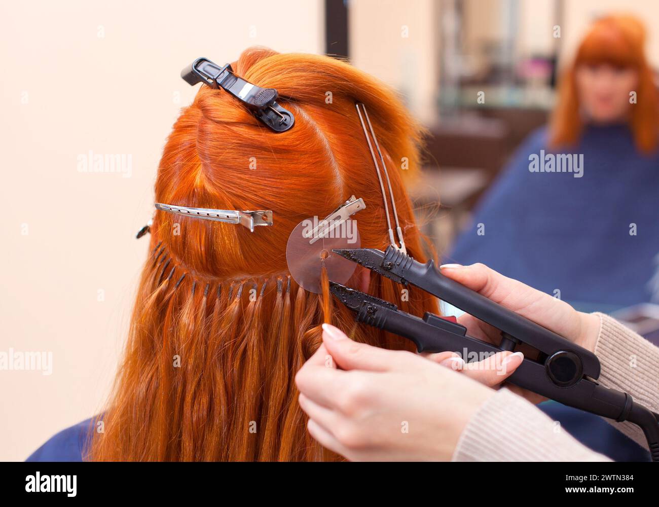 The hairdresser does hair extensions to a young, red-haired girl, in a beauty salon. Professional hair care. Stock Photo
