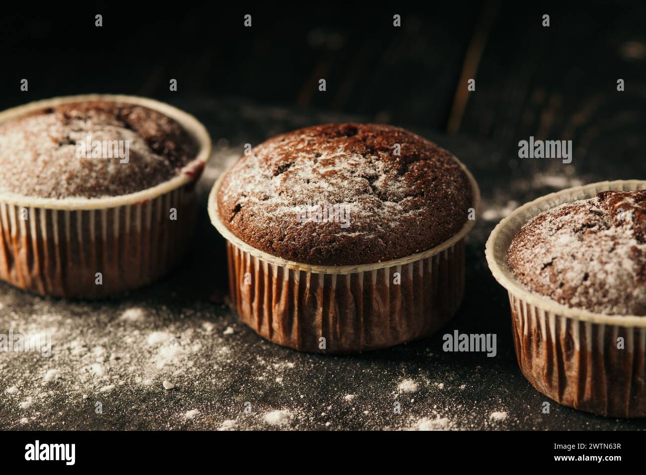 Chocolate muffins with powdered sugar on a black background. Still life close up. Dark moody. Food photo Stock Photo
