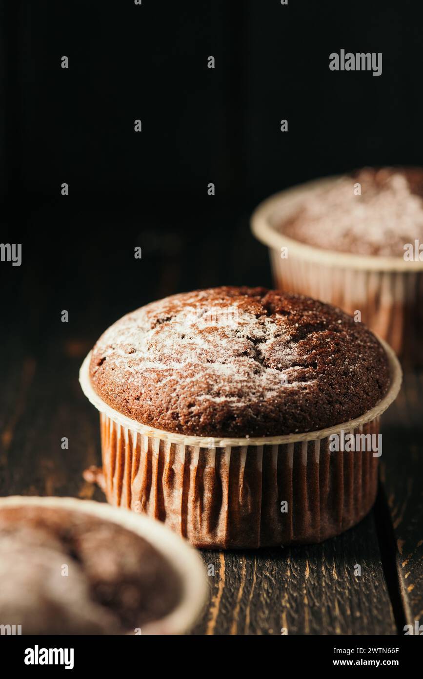 Chocolate muffins with powdered sugar on a black background. Still life close up. Dark moody. Food photo Stock Photo