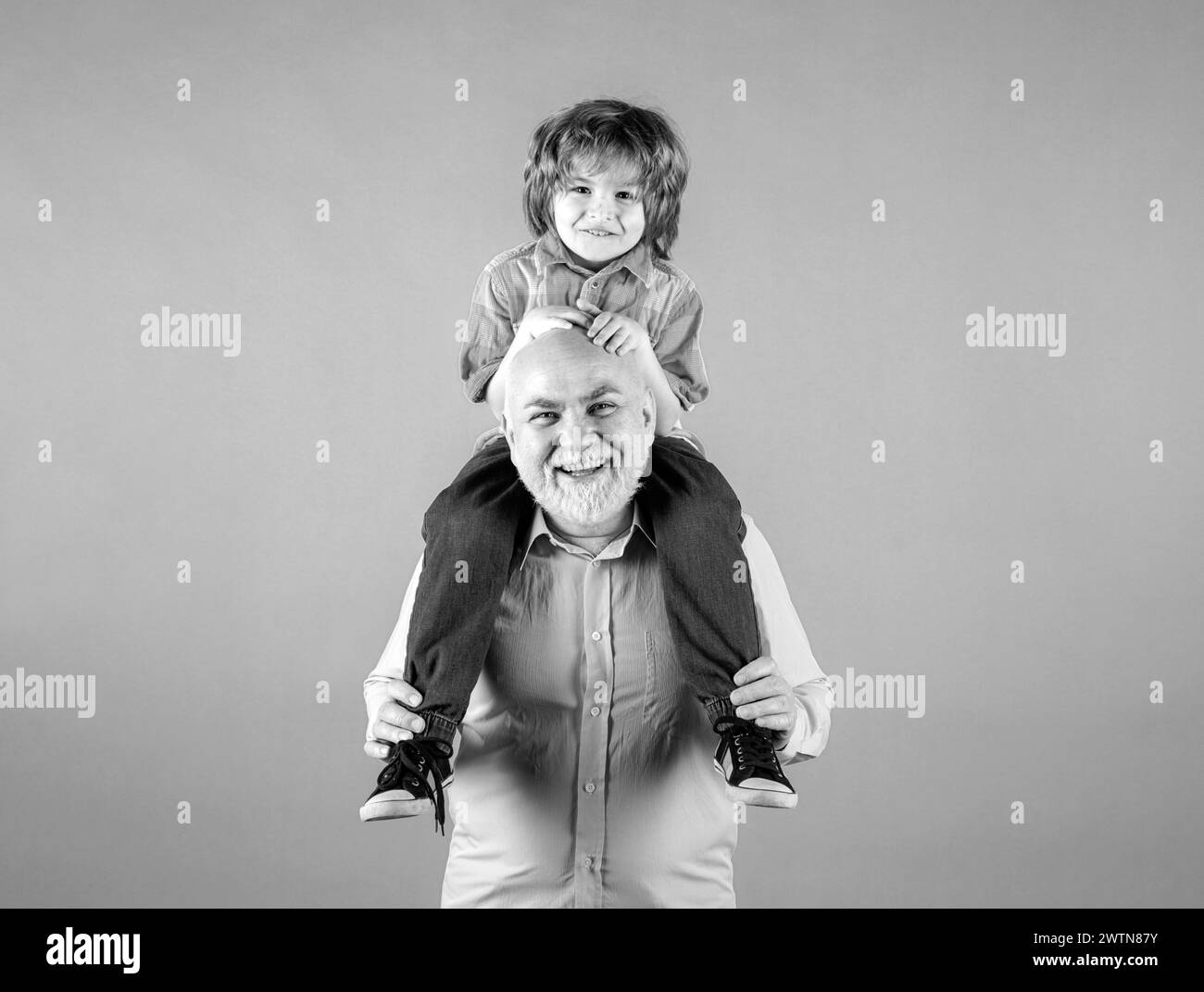 Grandfather and grandson piggy back ride with funny face isolated. Elderly old relative with child. Stock Photo