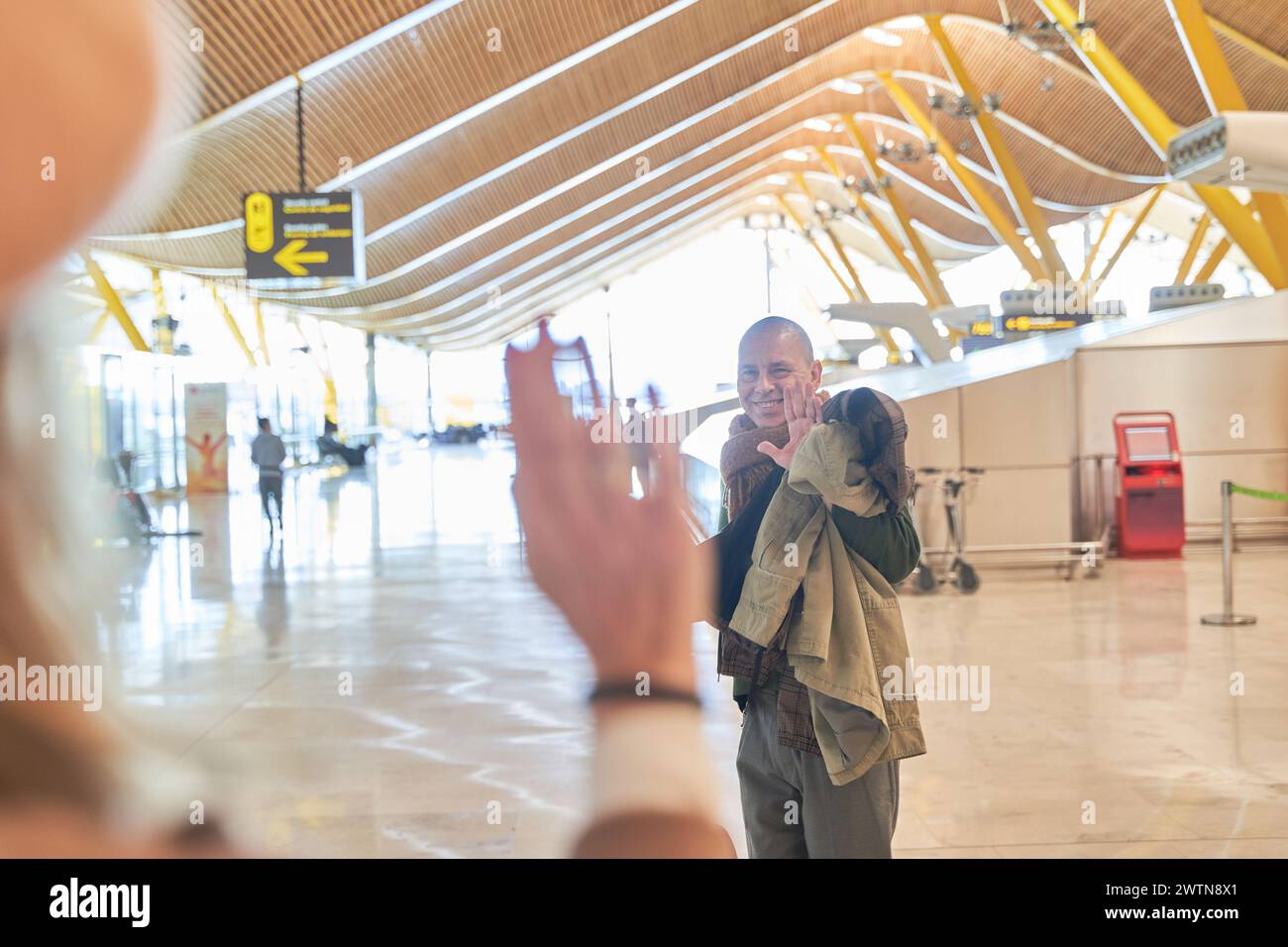 couple saying goodbye at airport. man waving goodbye to woman in foreground out of focus. Stock Photo