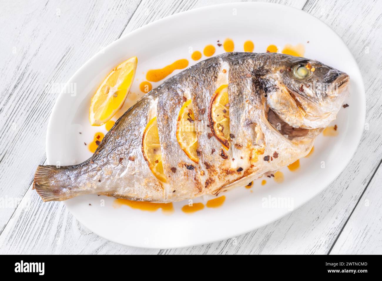 Baked dorado fish garnished with lemon and red oil Stock Photo
