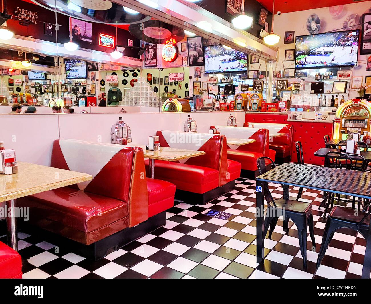 A retro, 1950's-style American diner with red vinyl booths and black and white checkered tile floors, and a jukebox at the back Stock Photo