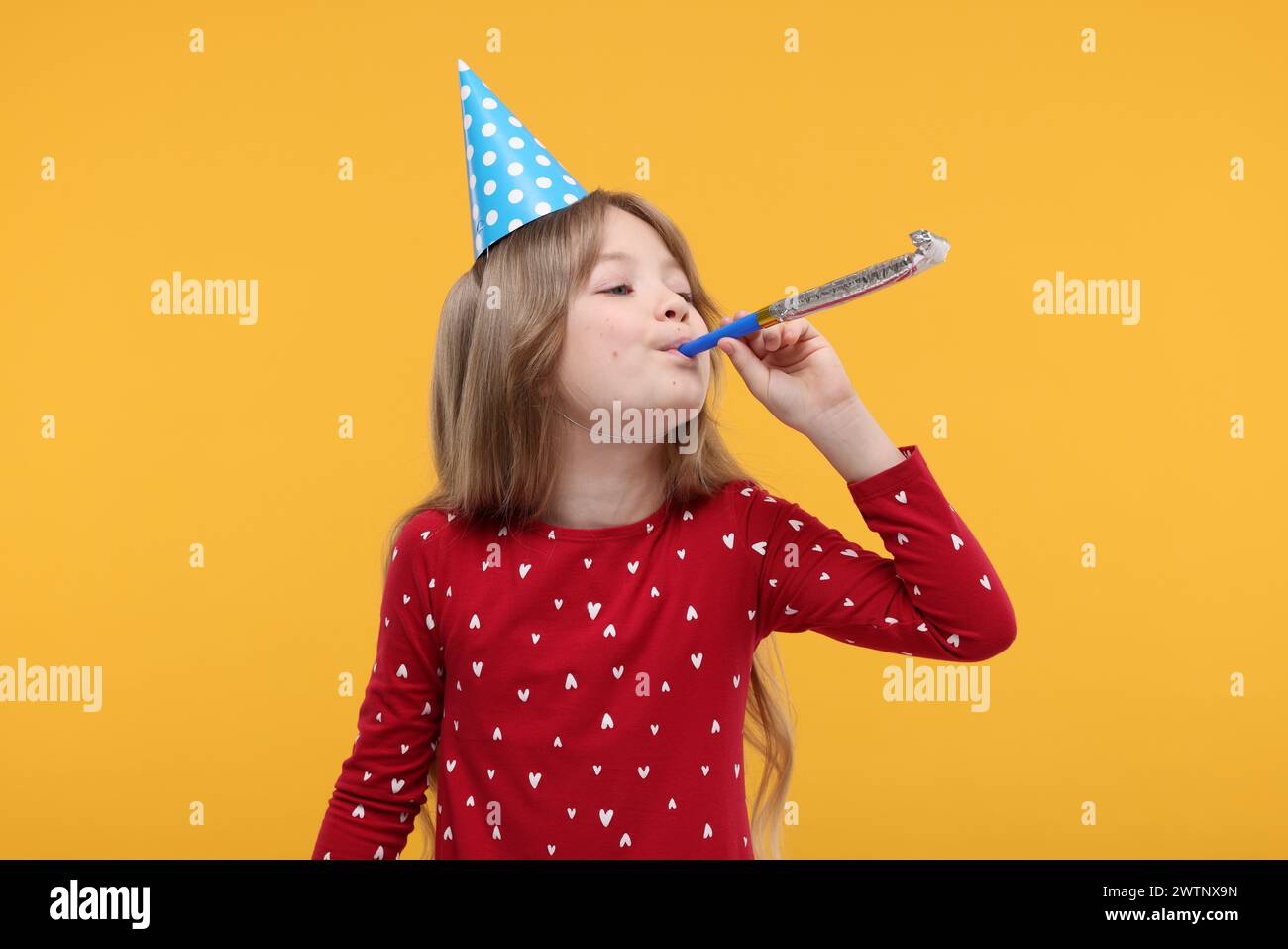 Cute little girl in party hat with blower on yellow background Stock ...
