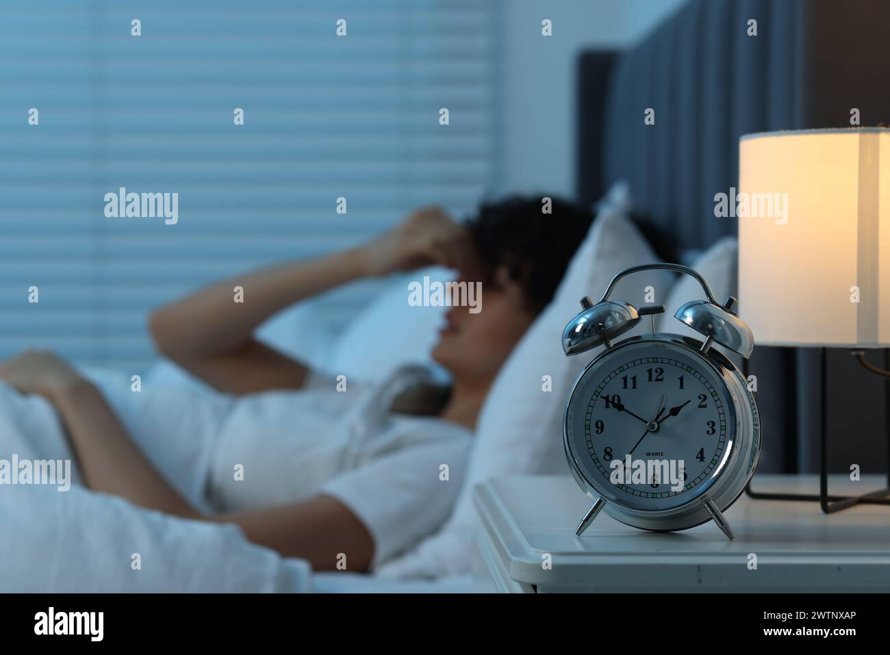 Young woman suffering from headache in bed at night, focus on alarm