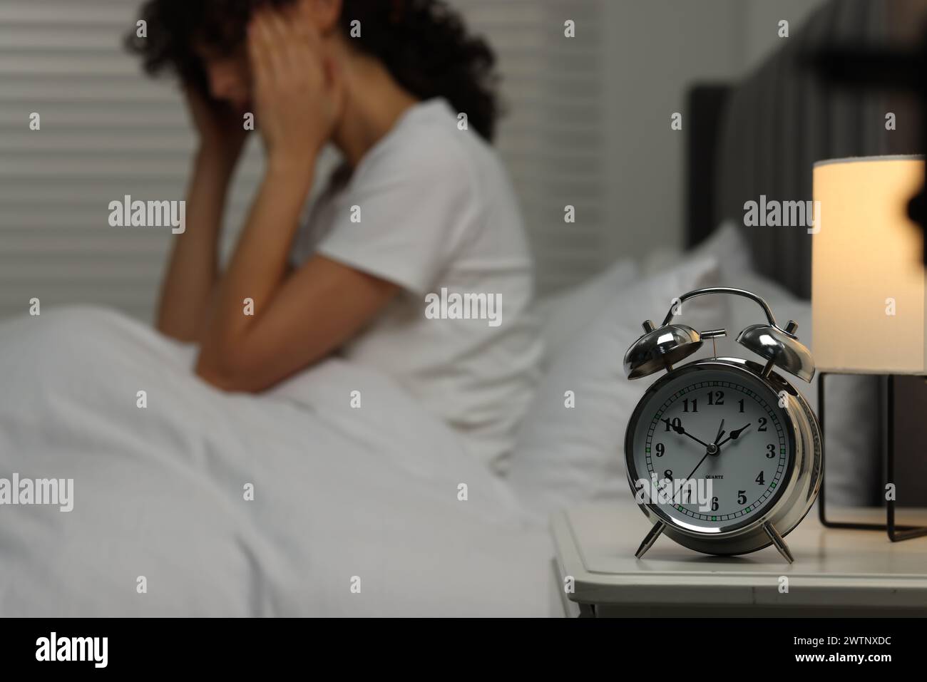 Woman suffering from headache in bed at night, focus on alarm clock