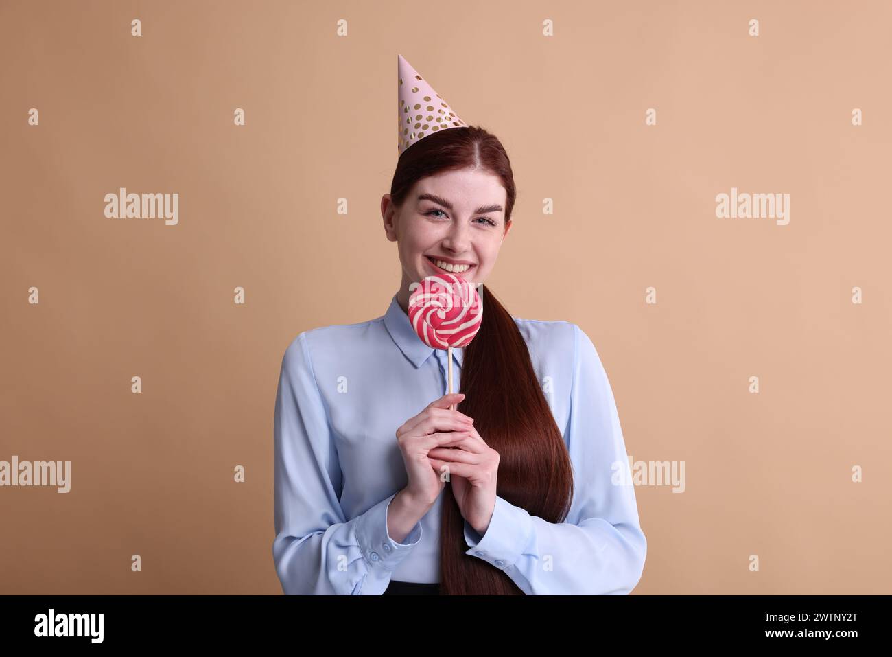 Happy woman in party hat with lollipop on beige background Stock Photo