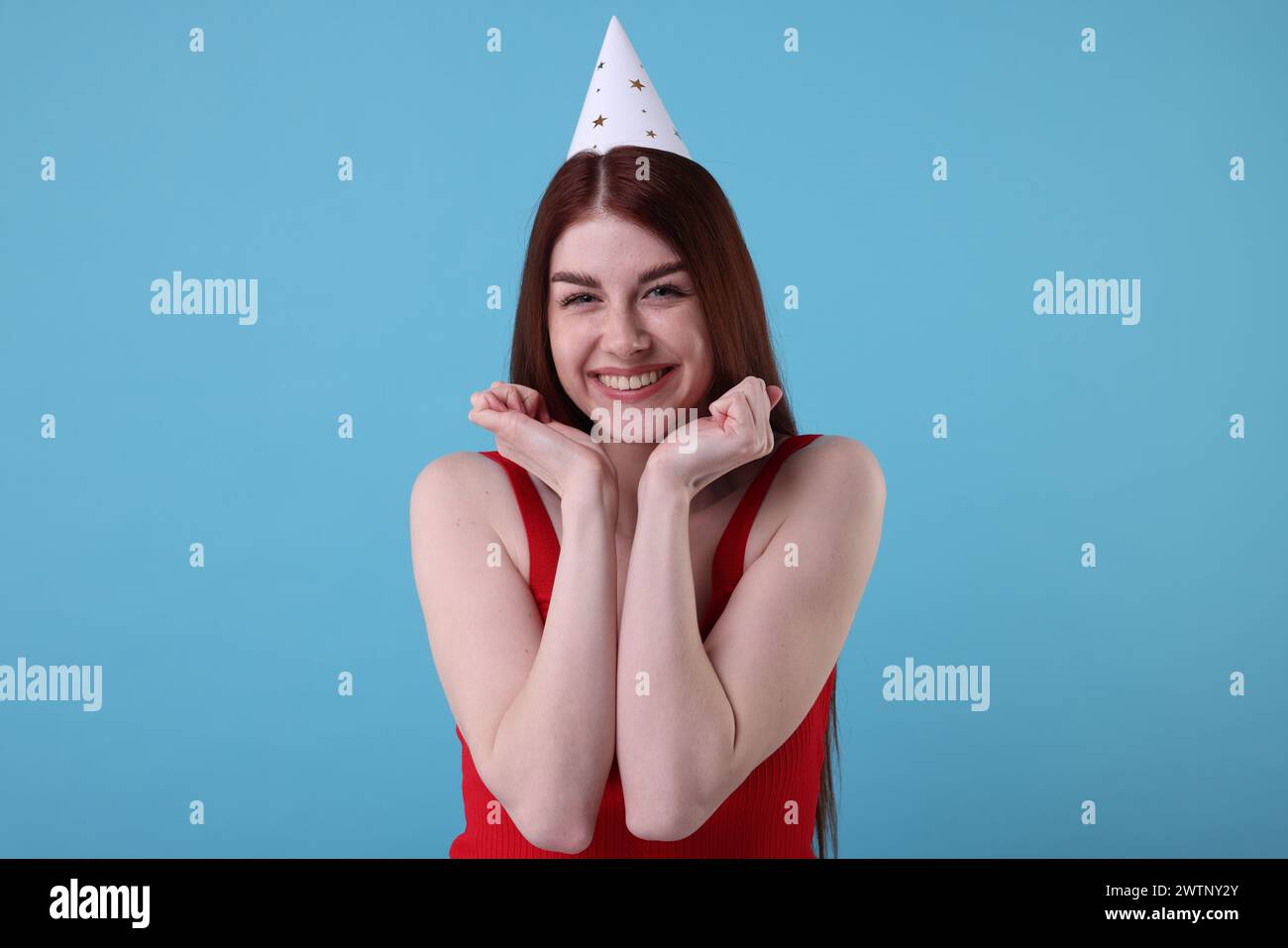 Happy woman in party hat on light blue background Stock Photo