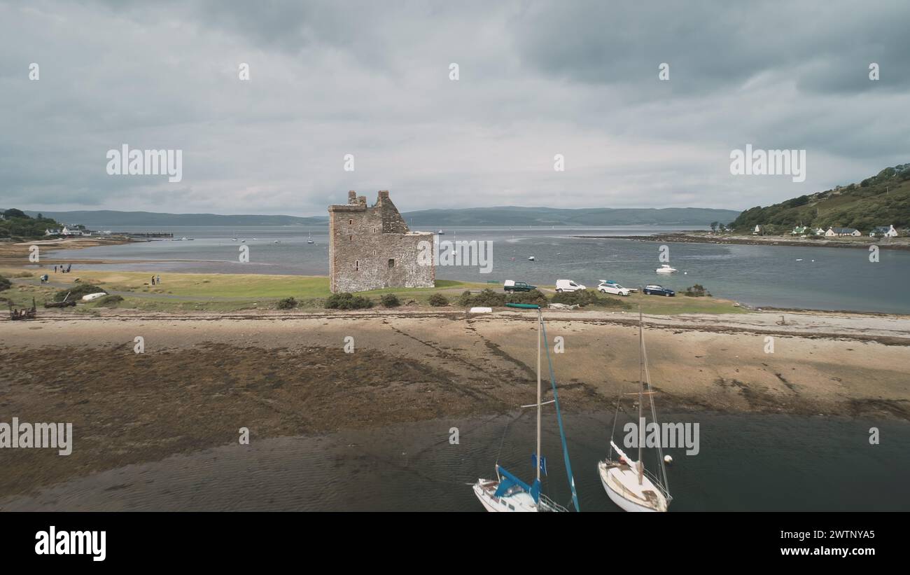 Scotland castle ruins aerial: ocean bay shore view. Historic Scottish Loch Ranza heritage. Magnificent landscape with ocean and mountains of Arran Island, United Kingdom. Footage Shot Stock Photo