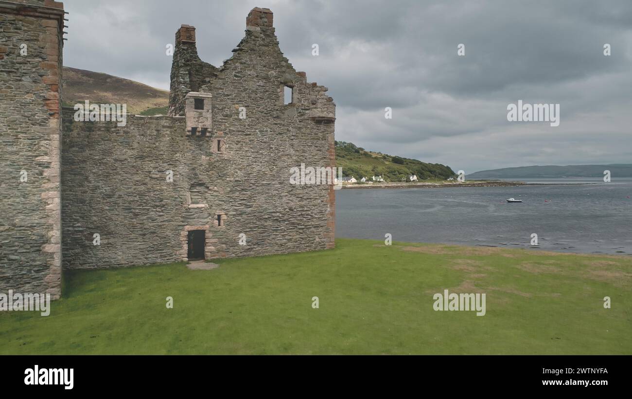 Closeup Scotland castle walls aerial shot seascape: dramatic scenery on summer cloudy day in front of bay. Majestic palace of Hamilton dynasty on coast of Arran Island, UK. Footage view Stock Photo