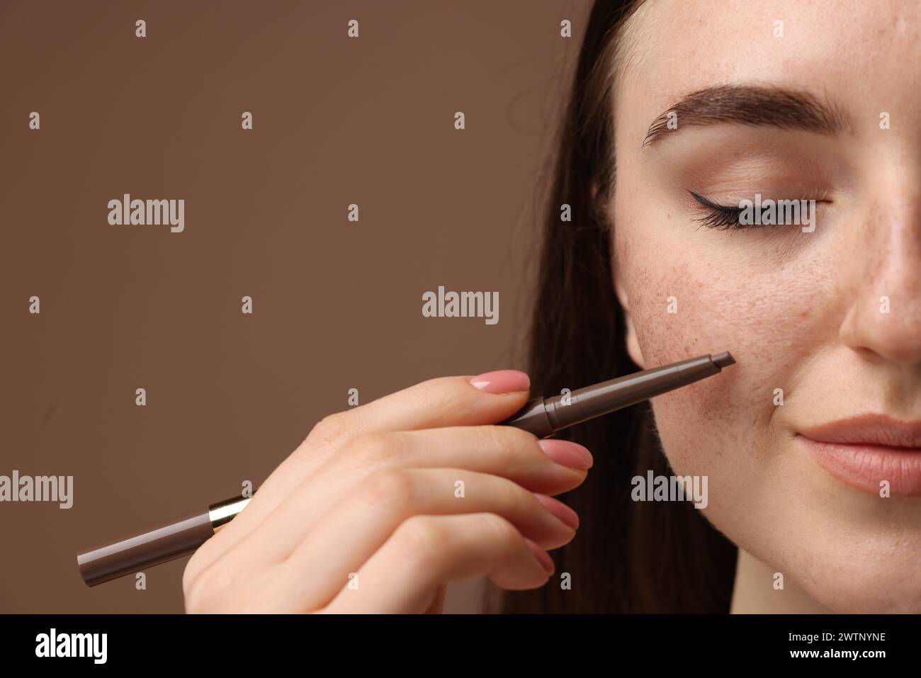 Beautiful woman drawing freckles with pen on brown background, closeup Stock Photo