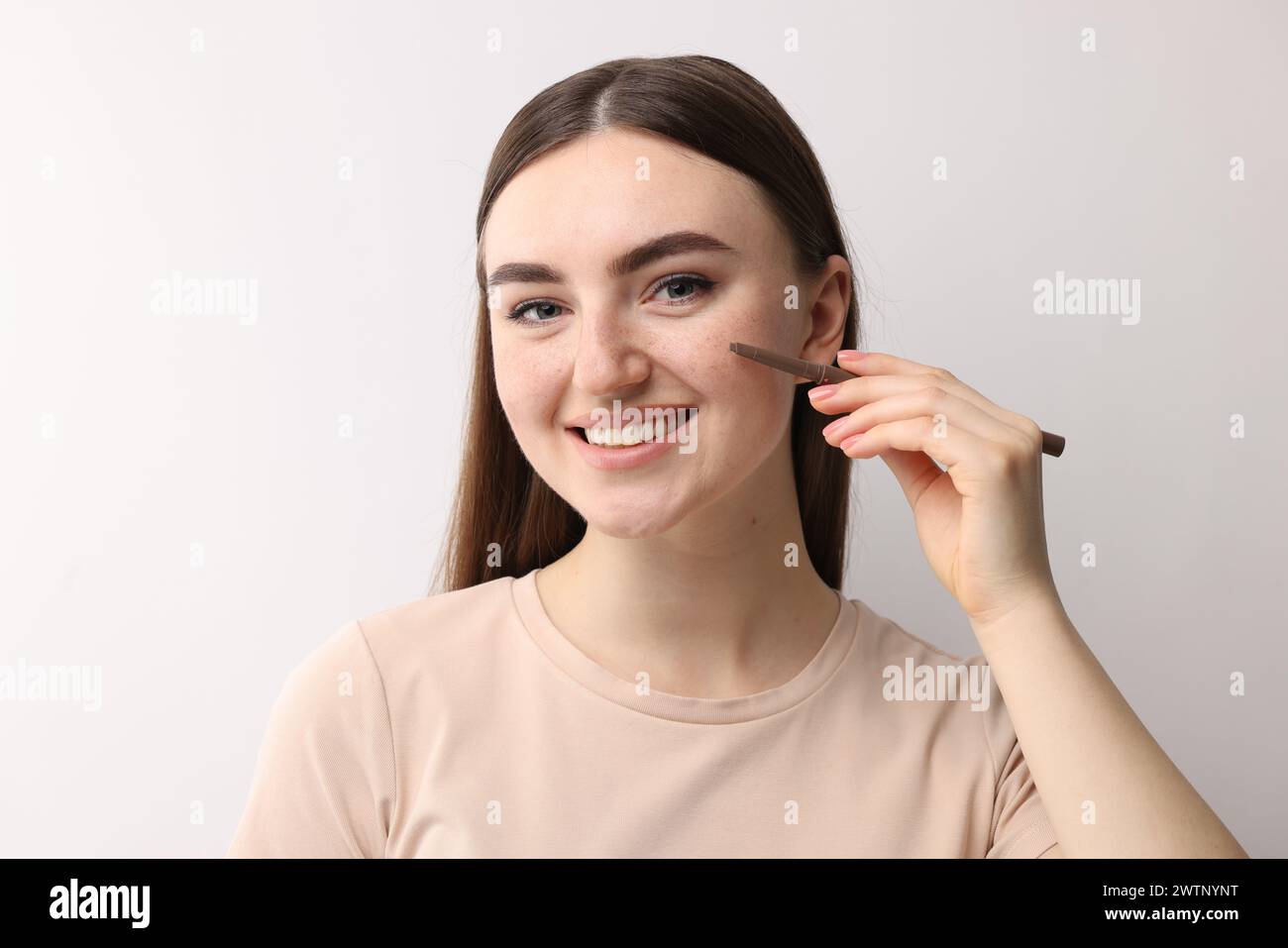 Smiling woman drawing freckles with pen on light background Stock Photo