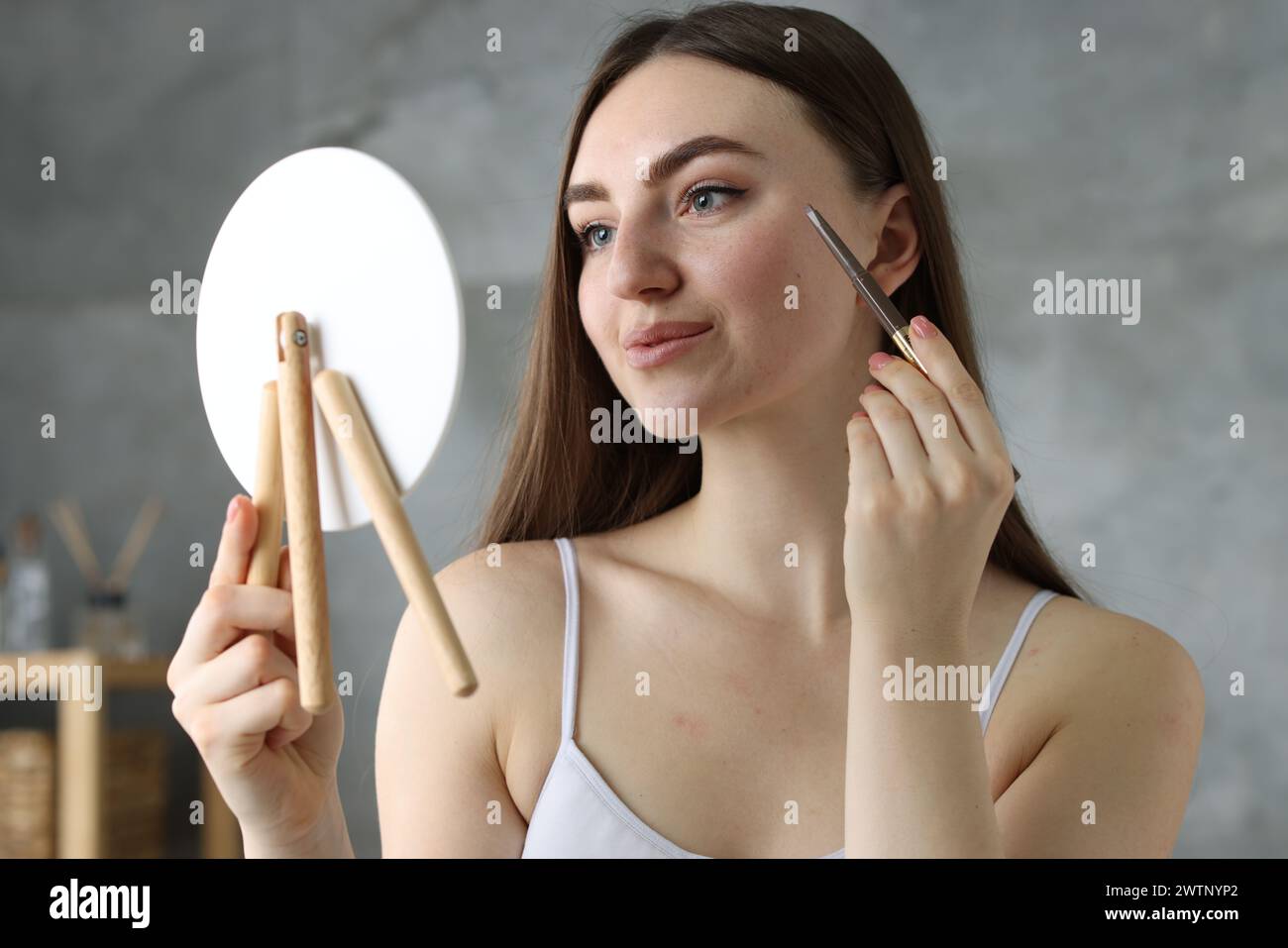 Beautiful woman drawing freckles with pen in front of little mirror indoors Stock Photo