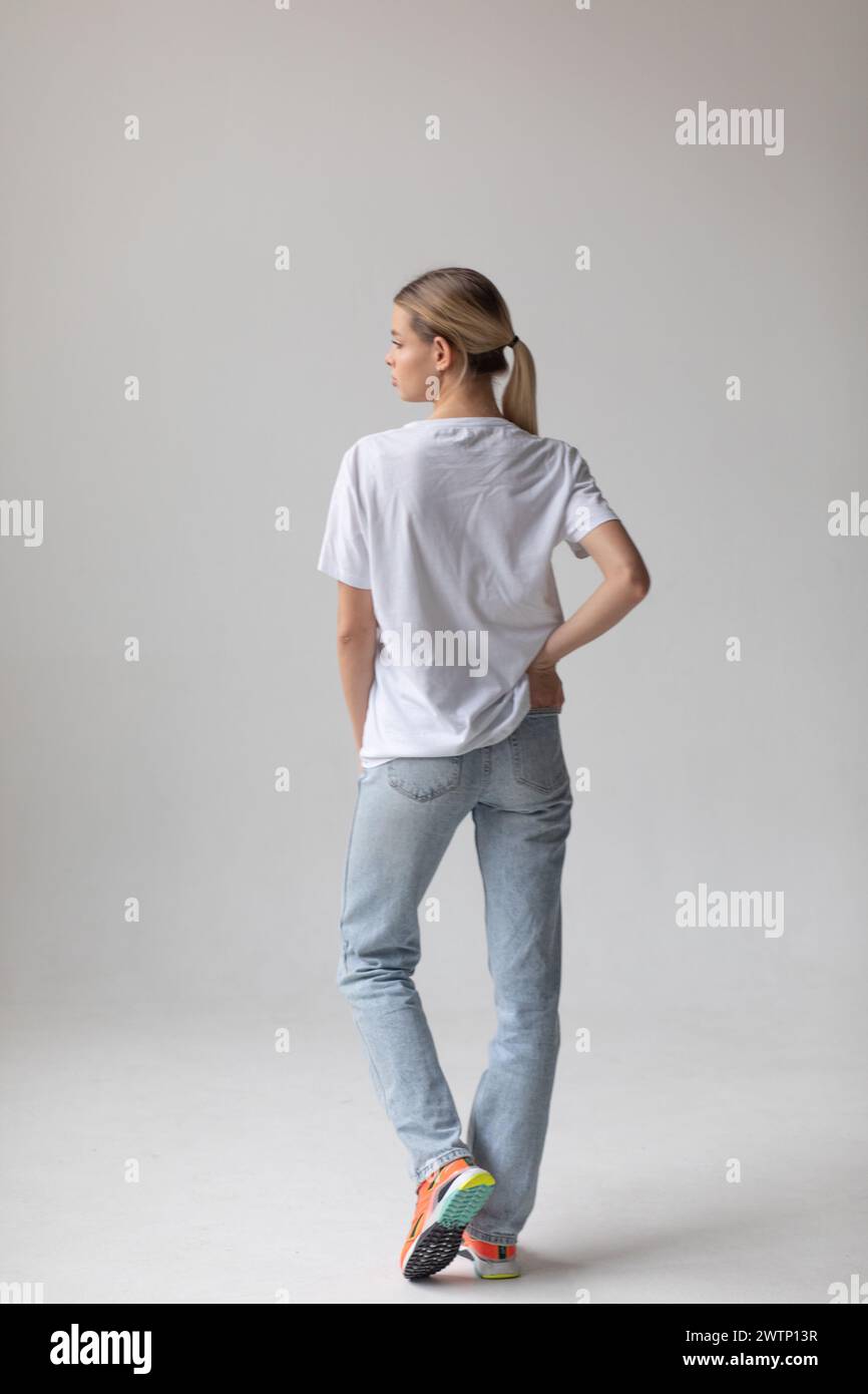 Beautiful blonde woman in a white T-shirt and blue jeans posing on a ...