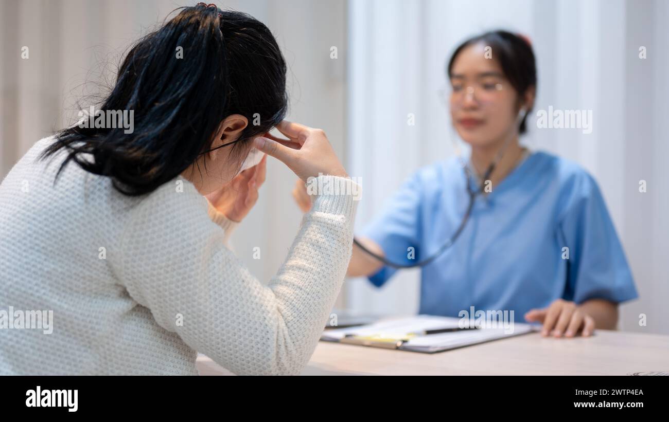 A stressed Asian female patient expressing concern about her health problems while discussing the treatment plan with a doctor at the hospital. health Stock Photo
