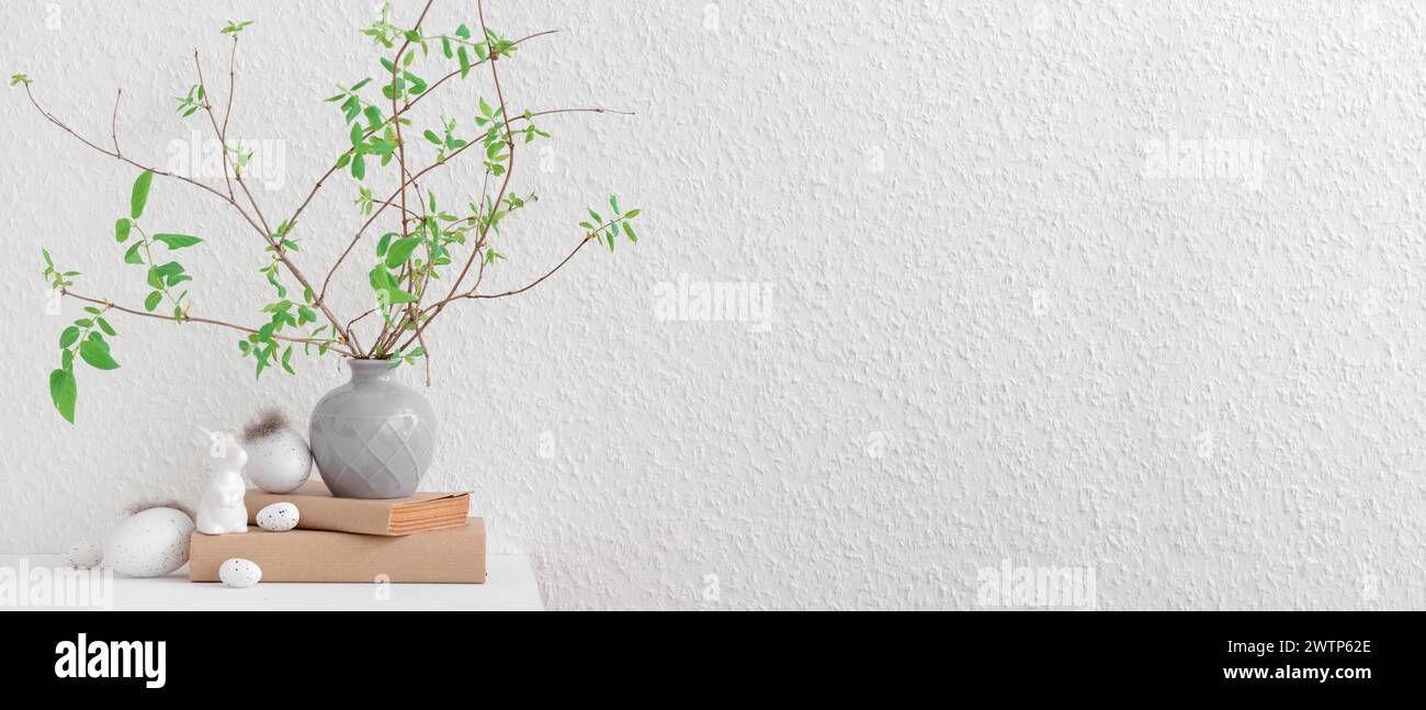 Vase with tree branches, Easter eggs and bunny on table near white wall ...