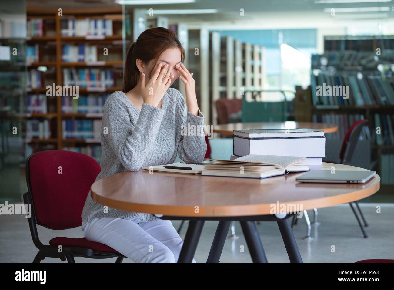 Young Asian woman student rubbing eyes, feeling tired after reading a book in library. Stock Photo