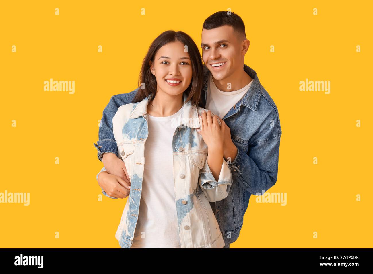 Young couple in stylish denim jackets hugging on yellow background Stock Photo
