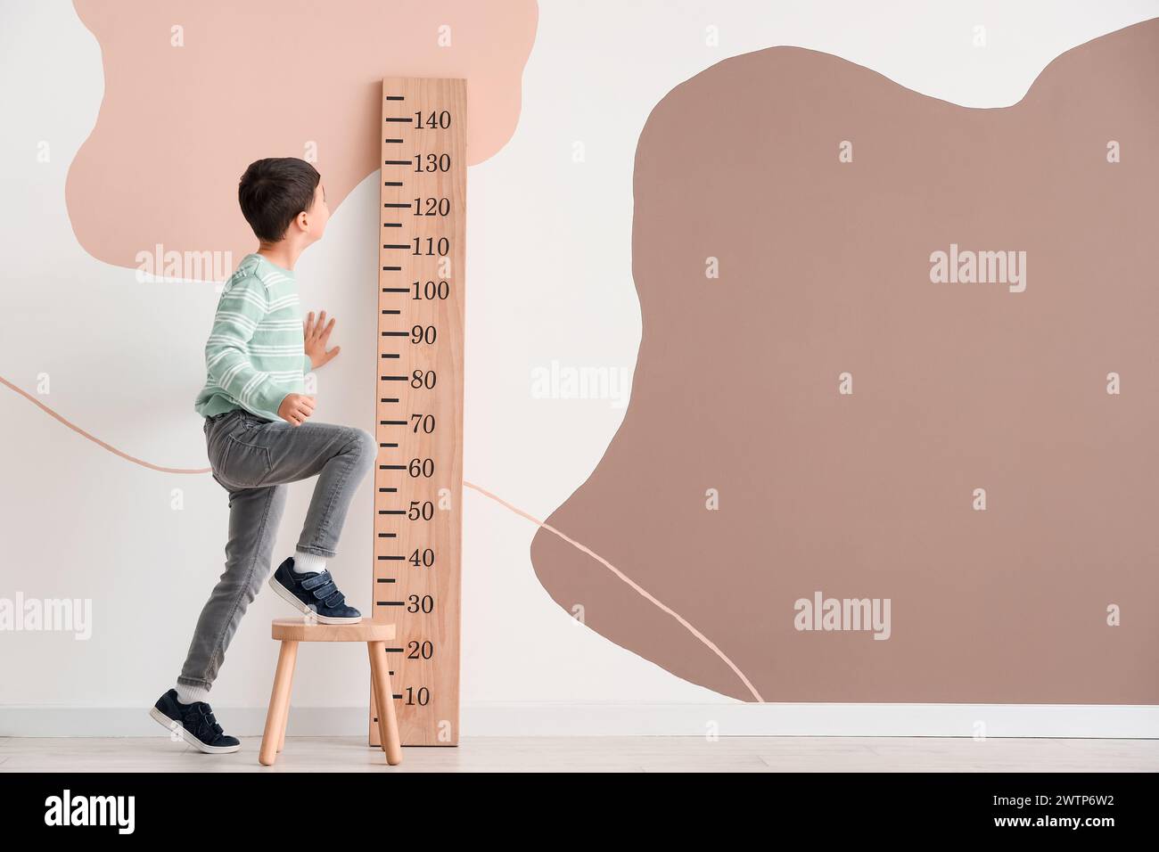 Cute little boy on stool measuring height near wooden stadiometer at home Stock Photo