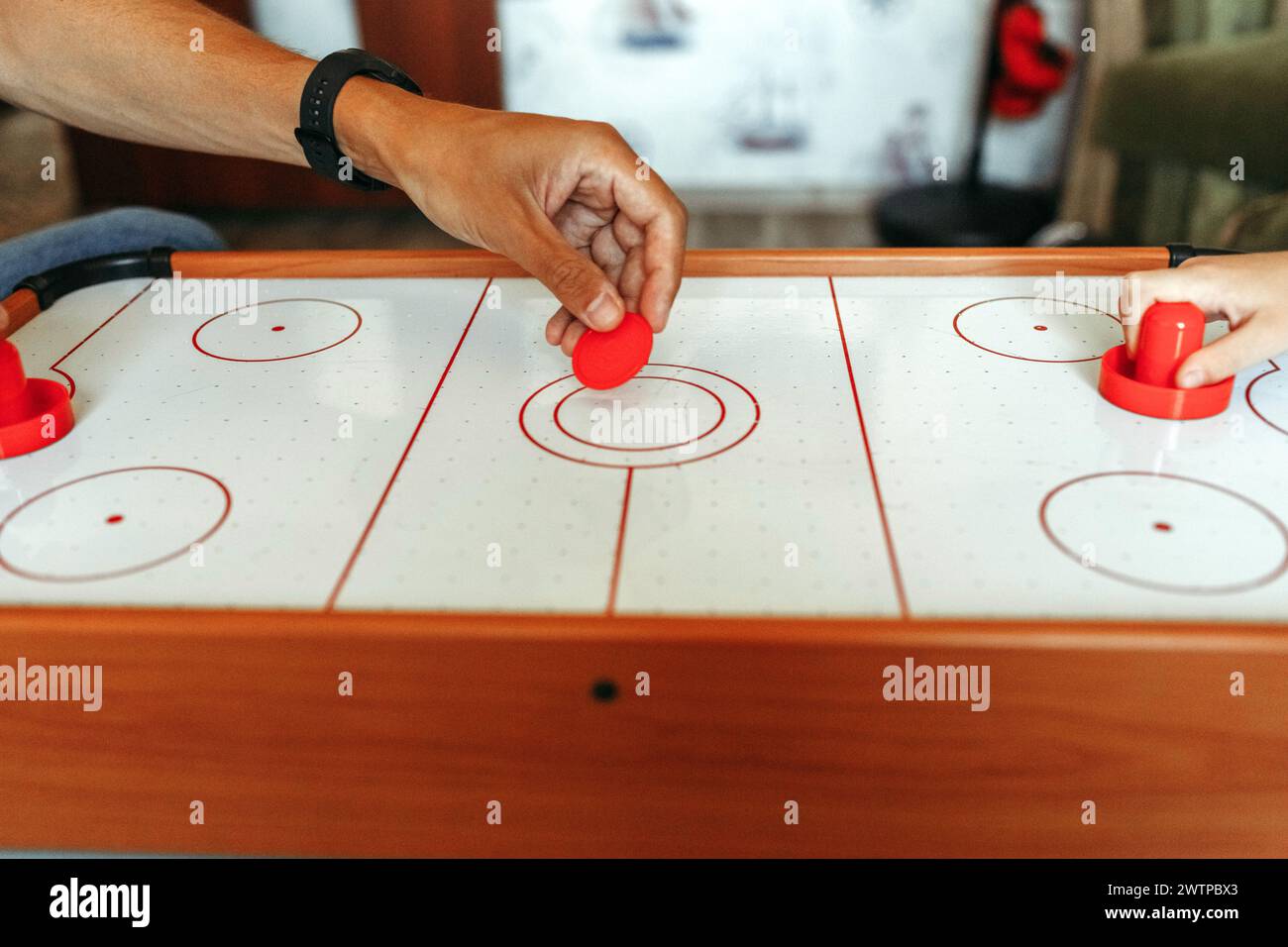 Two individuals engaged in a game of air hockey, skillfully striking the puck with paddles on a smooth table surface. Stock Photo