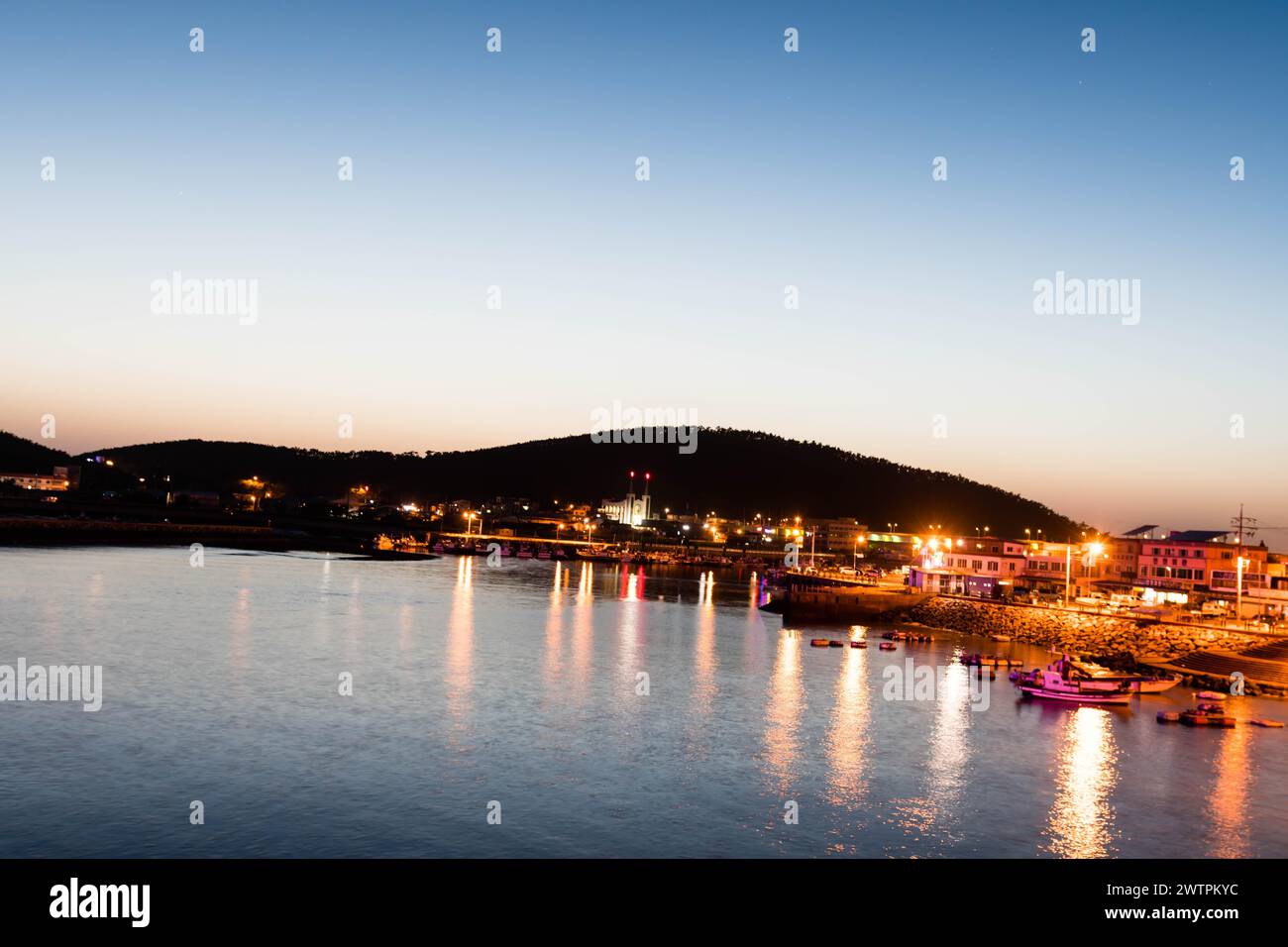 Serene harbor scene at twilight with boats, calm water, and a hill in the background, in Sinjin-do, South Korea, Asia Stock Photo