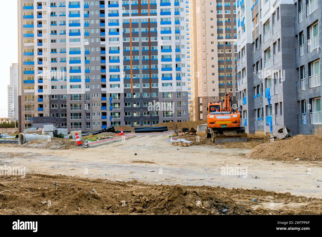 Orange excavator on a dirt road with newly constructed high-rise apartment buildings, in Daejeon, South Korea Stock Photo