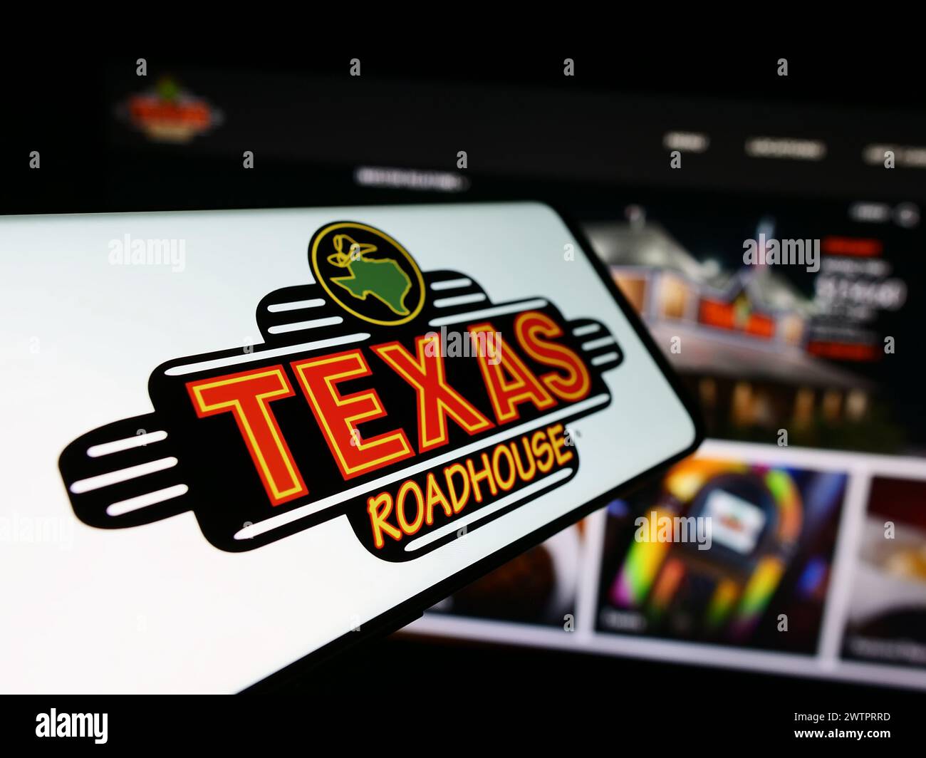 Mobile phone with logo of American steakhouse restaurant company Texas Roadhouse Inc. in front of website. Focus on left of phone display. Stock Photo