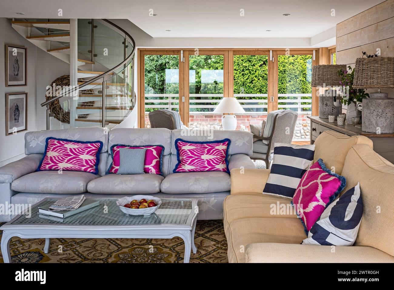 Bright pink cushions on sofas with spiral staircase in British home in Blakeney, Norfolk, UK Stock Photo