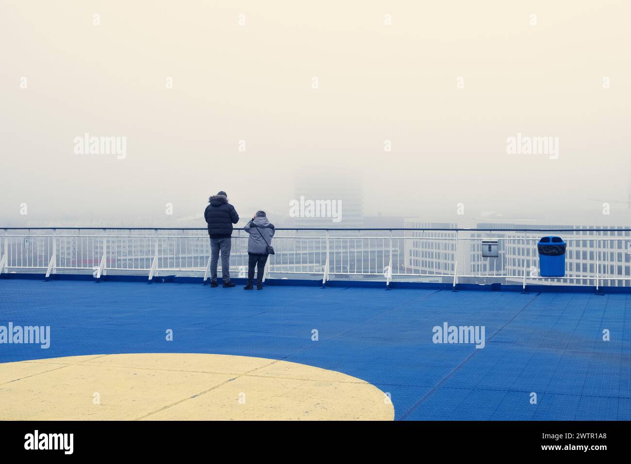 A rear view of passengers on a ferry deck observe mist enveloping the surroundings Stock Photo