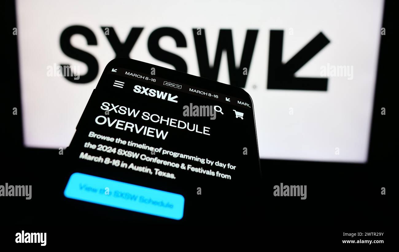 Smartphone with website of annual film and media event South by Southwest (SXSW) in front of logo. Focus on top-left of phone display. Stock Photo