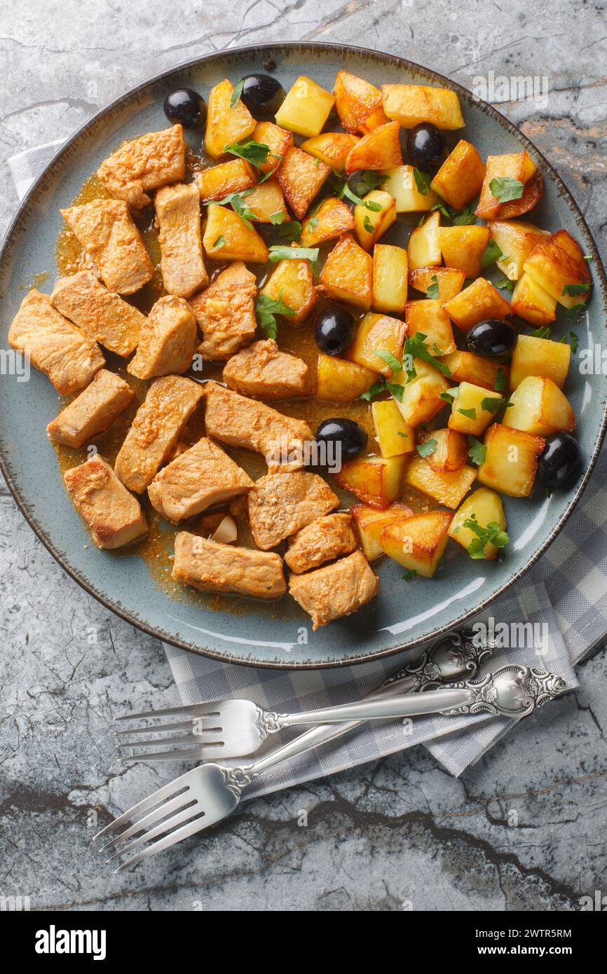 Rojoes Minhota Portuguese pork stew with fried potato and olive closeup on the plate on the table. Vertical top view from above Stock Photo