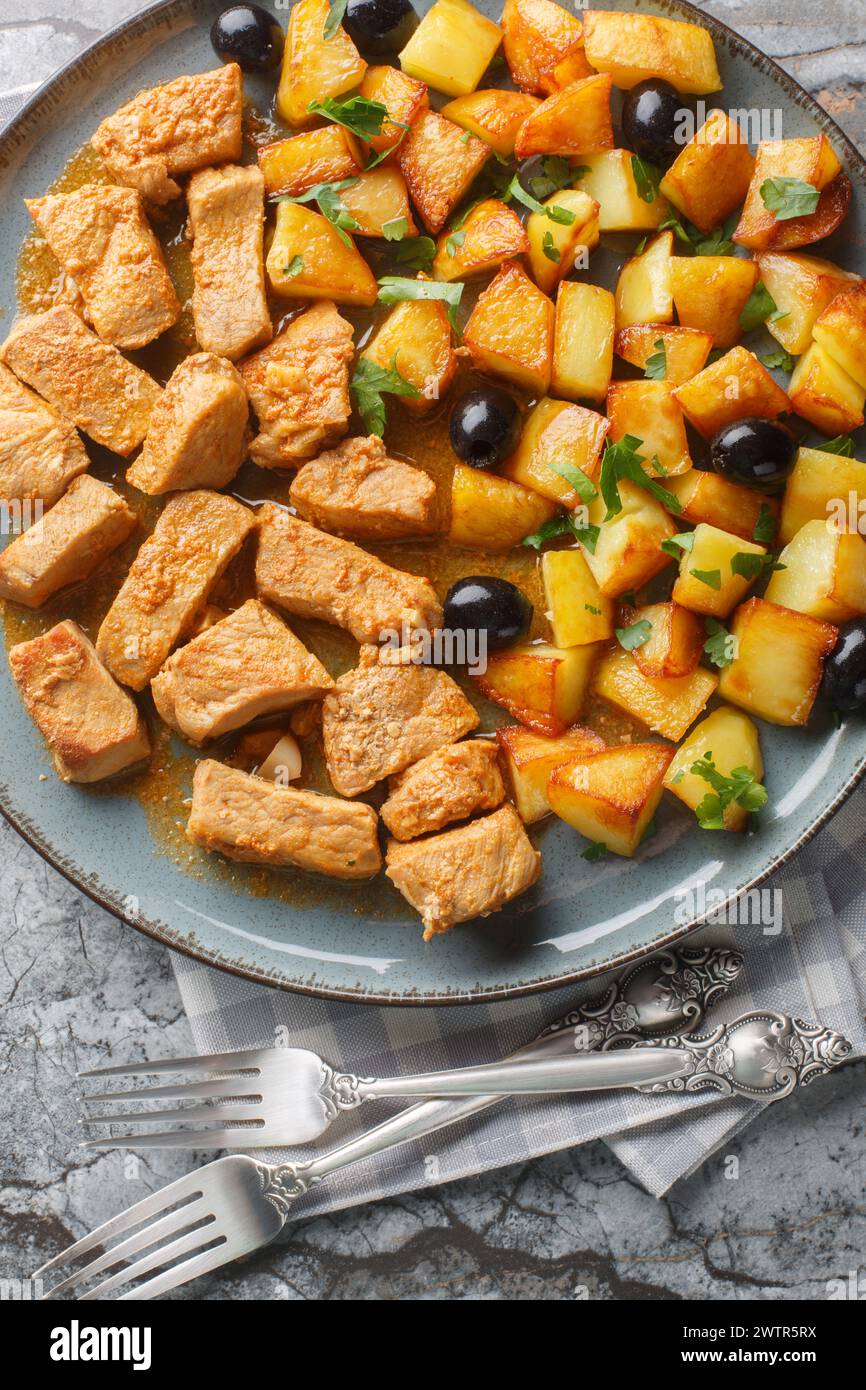 Portuguese Rojoes marinated pork then fried and stewed served with fried potatoes and olives close up in a plate on the table. Vertical top view from Stock Photo
