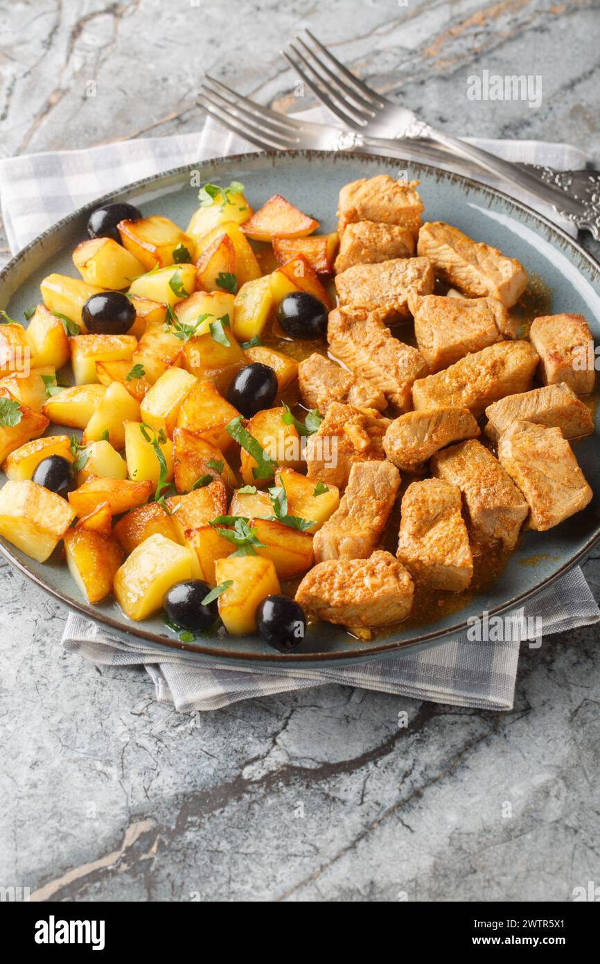 Rojoes Minhota Portuguese pork stew with fried potato and olive closeup on the plate on the table. Vertical Stock Photo