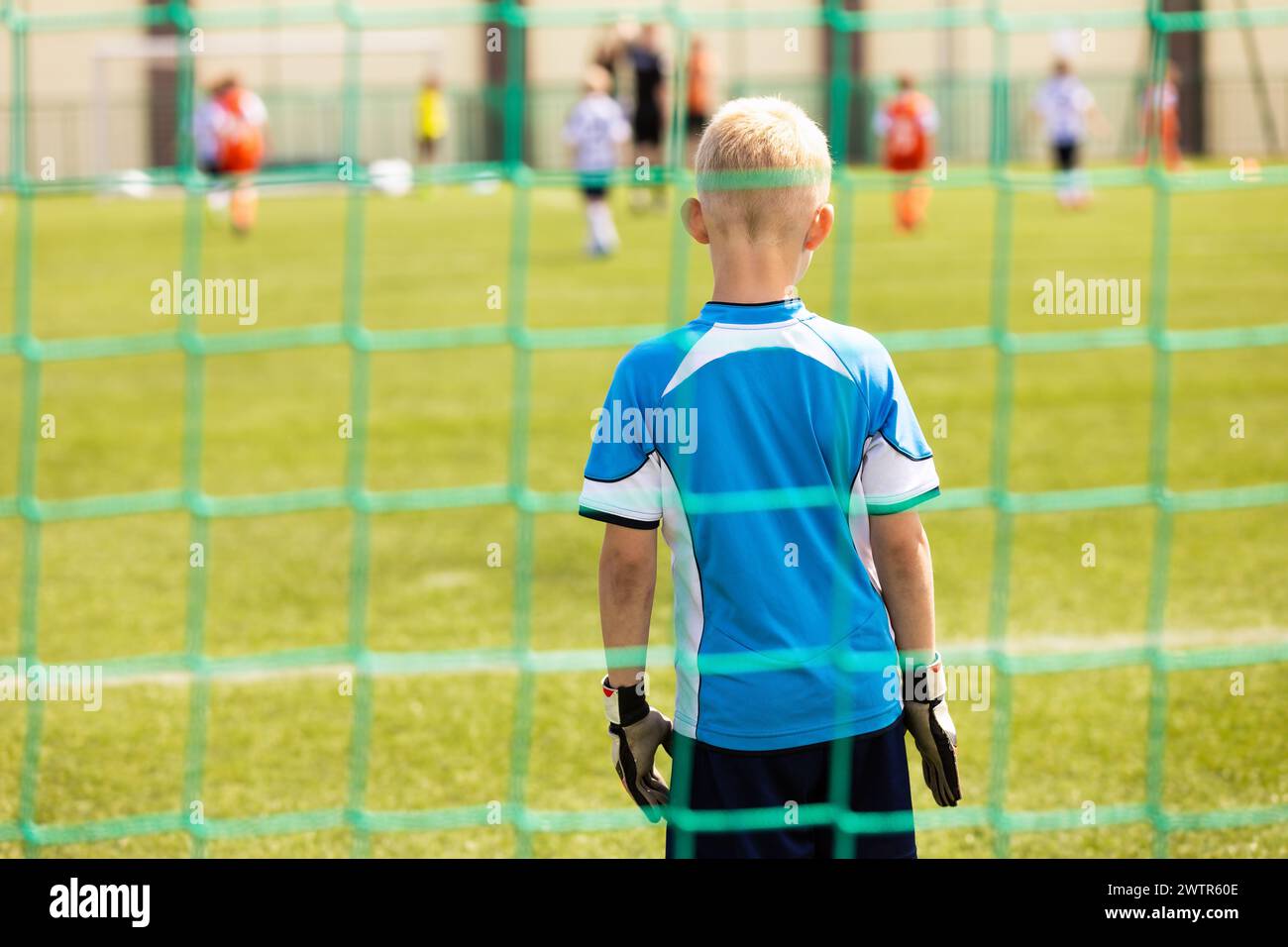 Little Boy in Goalkeeper Uniform and Gloves Standing in a Soccer Goal. Kids Play Football Game on School Sports Pitch Stock Photo
