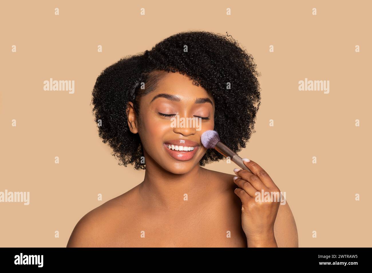 Joyful black woman applying blush, makeup routine joy Stock Photo Alamy
