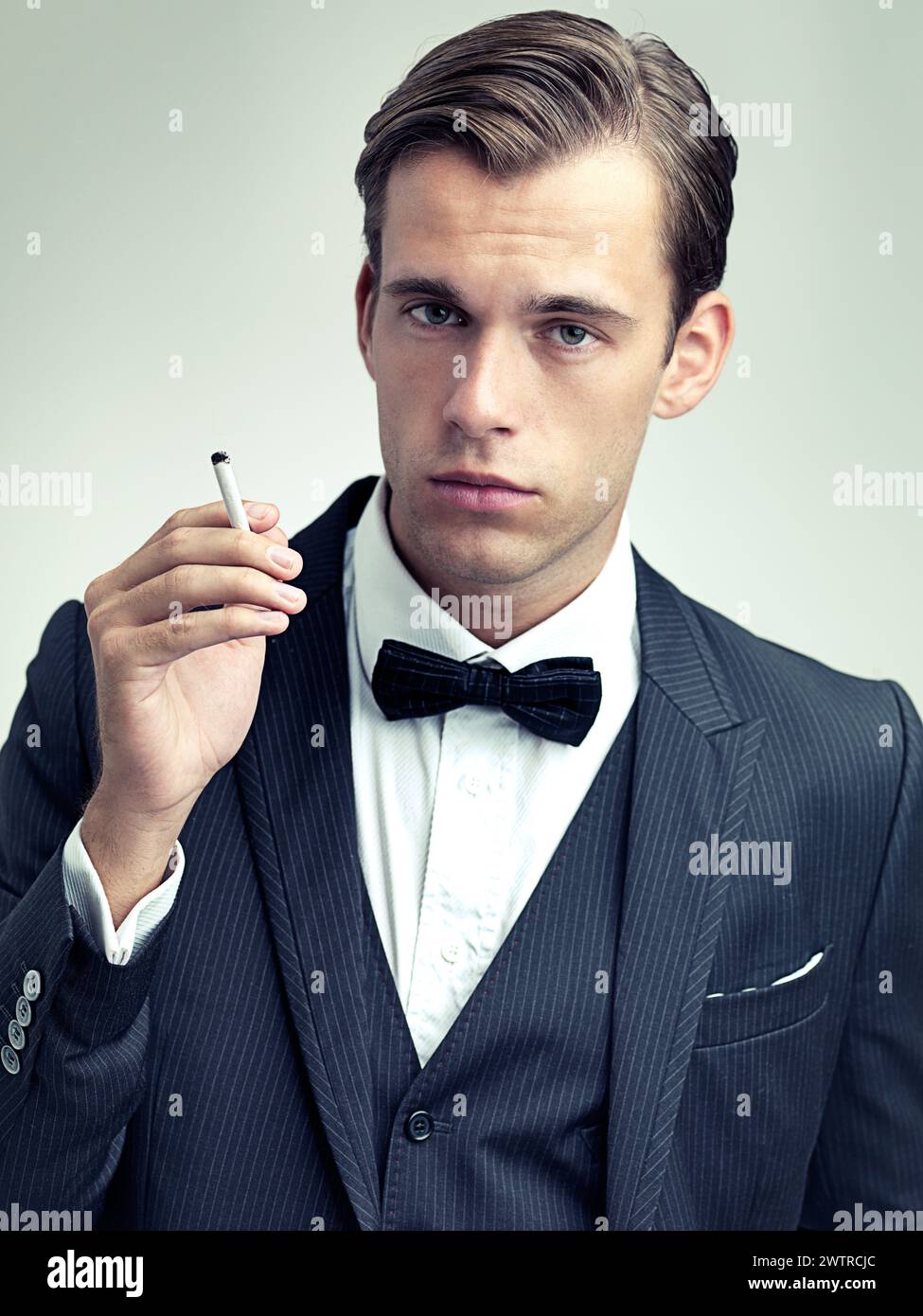 elegant cigarette Portrait, elegant or young gentleman smoking a cigarette in studio,  confidence or vintage fashion by white background. Face, serious and man in  retro Stock Photo