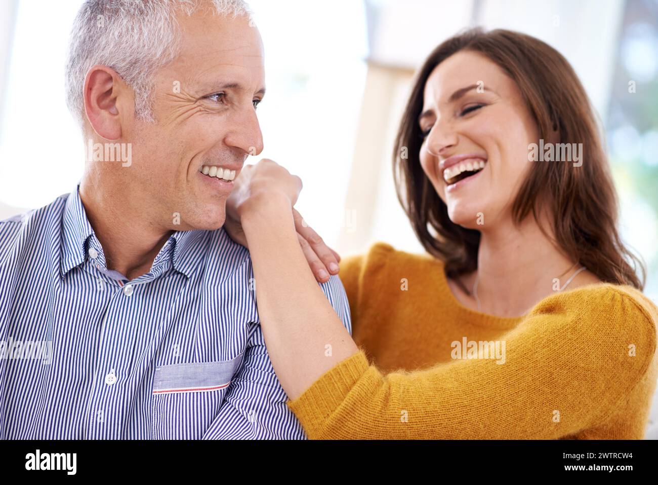 Couple, happy and laughing in home for hug with support, funny joke and romance in living room of house. Senior man, woman and comic with face for Stock Photo