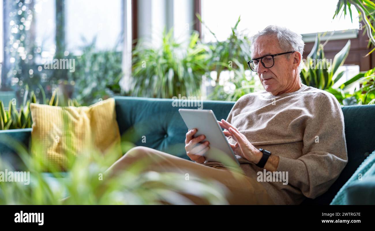 Senior man using digital tablet while sitting on sofa in living room at home Stock Photo