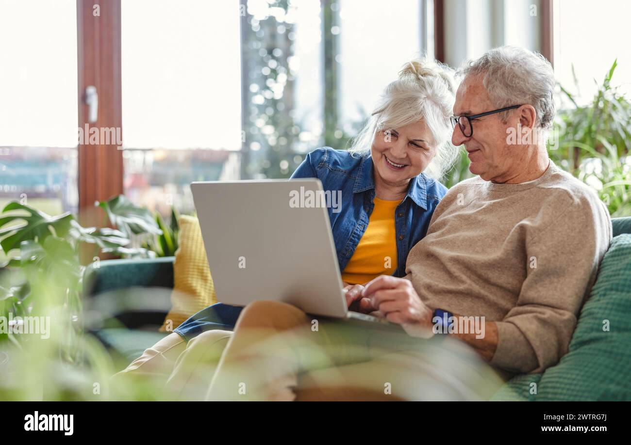 Senior couple using laptop while sitting on sofa in living room at home Stock Photo
