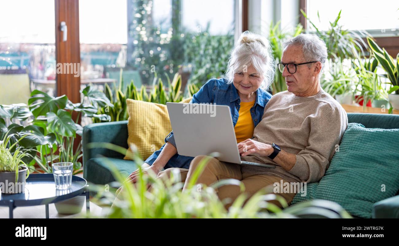 Senior couple using laptop while sitting on sofa in living room at home Stock Photo